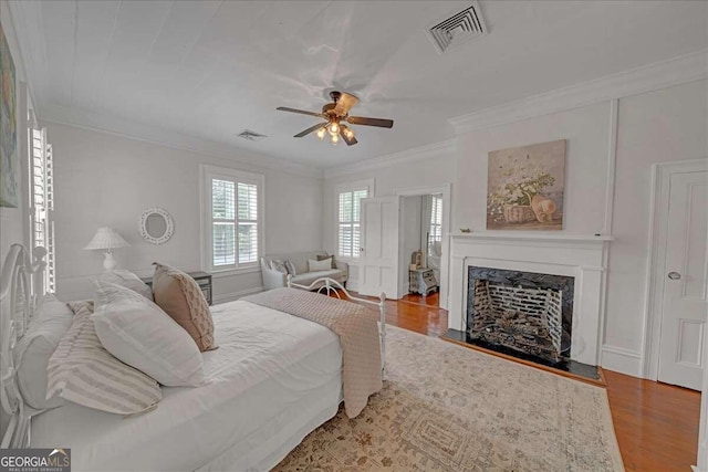 bedroom with ceiling fan, crown molding, wood-type flooring, and a fireplace