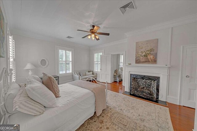 bedroom with visible vents, wood finished floors, a fireplace, and ornamental molding