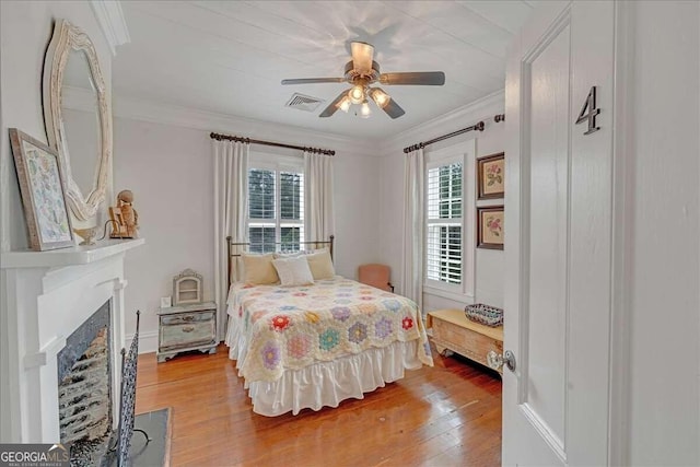 bedroom featuring a ceiling fan, visible vents, a fireplace with flush hearth, crown molding, and light wood-type flooring