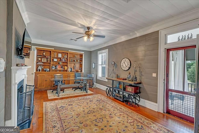 office area with a fireplace, crown molding, a ceiling fan, and wood finished floors
