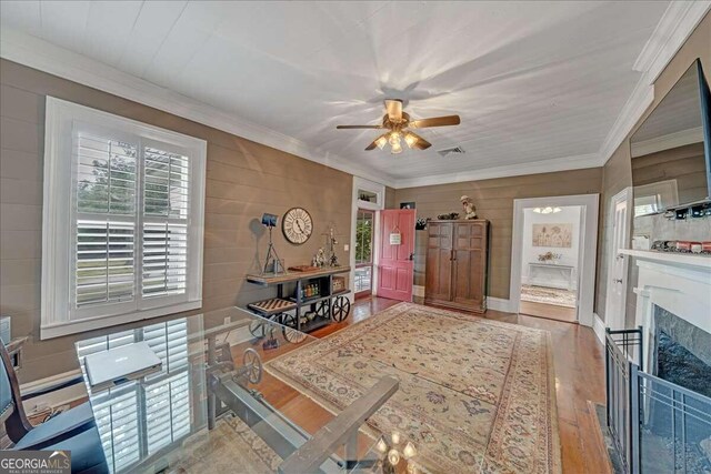 interior space featuring wood finished floors, visible vents, a fireplace, ceiling fan, and crown molding