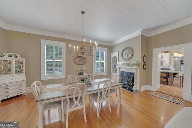 dining room with baseboards, a fireplace with flush hearth, light wood-style floors, crown molding, and a chandelier