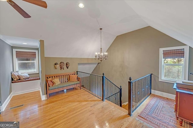 stairway featuring visible vents, ceiling fan with notable chandelier, wood finished floors, baseboards, and vaulted ceiling