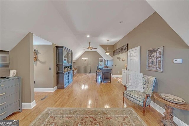 sitting room with light wood-type flooring, an upstairs landing, baseboards, and vaulted ceiling