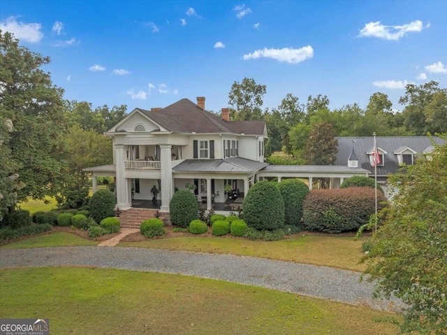 view of front of home featuring a chimney, a balcony, a porch, and a front yard