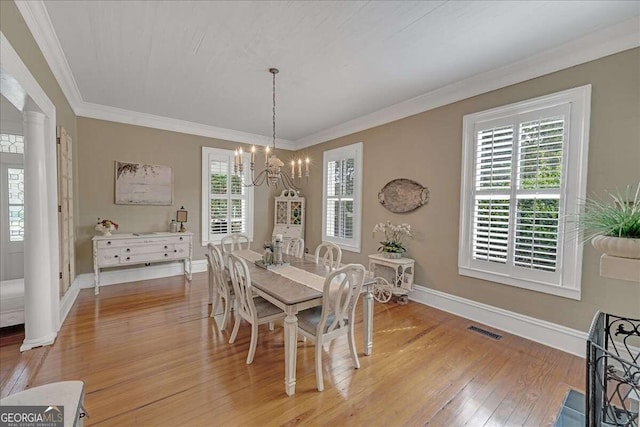 dining area with baseboards, visible vents, light wood-style flooring, crown molding, and a chandelier