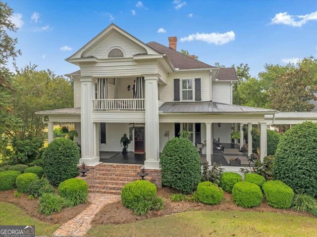 rear view of property with a balcony, a standing seam roof, covered porch, a chimney, and metal roof