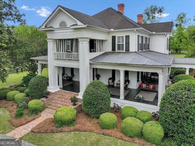 back of property featuring a balcony, a porch, a chimney, and a shingled roof