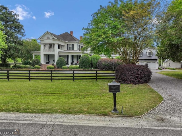 neoclassical home with a fenced front yard, a balcony, a chimney, and a front yard