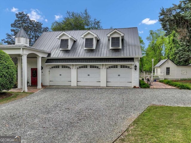 view of front facade with a standing seam roof, metal roof, gravel driveway, and a garage