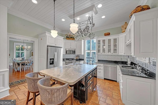 kitchen with a kitchen island with sink, hanging light fixtures, decorative backsplash, appliances with stainless steel finishes, and white cabinetry