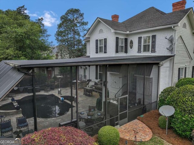 view of front of property featuring a fenced in pool, roof with shingles, a chimney, a sunroom, and a patio area