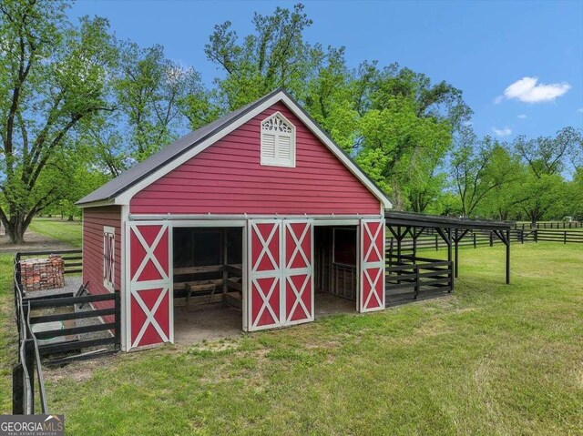 view of barn with an exterior structure, a lawn, and fence