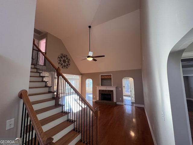 staircase with ceiling fan, a fireplace, high vaulted ceiling, and hardwood / wood-style floors