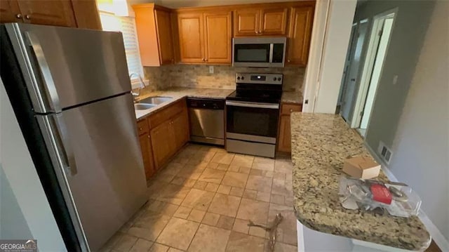 kitchen with sink, light stone counters, stainless steel appliances, and tasteful backsplash