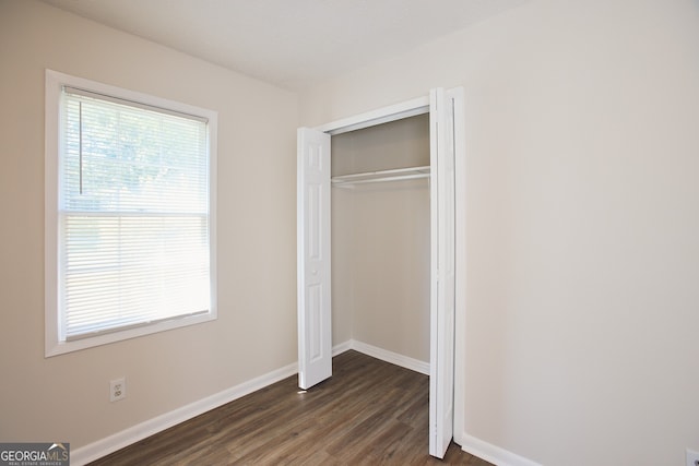 unfurnished bedroom with multiple windows, a closet, and dark wood-type flooring