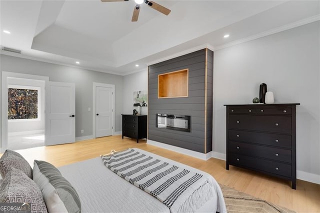 bedroom featuring a raised ceiling, ceiling fan, crown molding, a fireplace, and light hardwood / wood-style floors