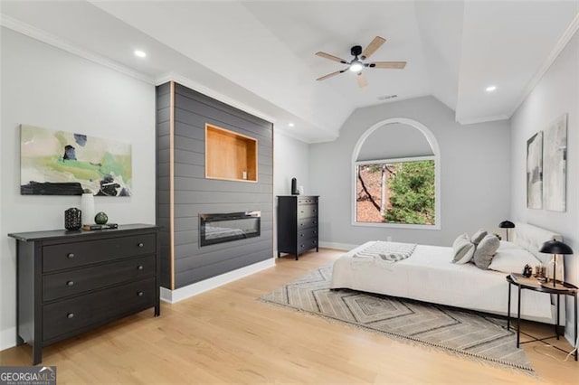 bedroom with ceiling fan, a large fireplace, light hardwood / wood-style flooring, lofted ceiling, and ornamental molding