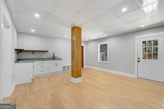 bar featuring light stone counters, white cabinetry, sink, and light hardwood / wood-style flooring