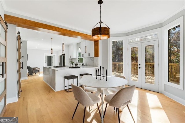 dining space with light hardwood / wood-style floors, a barn door, ornamental molding, and french doors