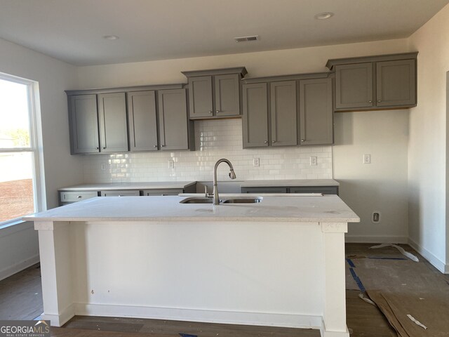 kitchen with gray cabinetry, sink, backsplash, a breakfast bar area, and a kitchen island with sink