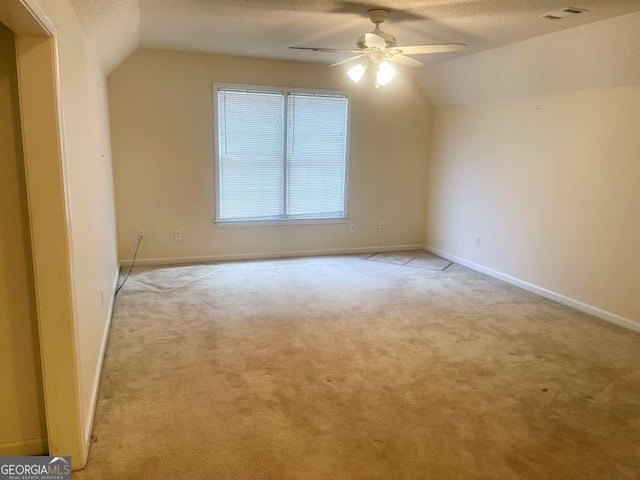 empty room featuring a textured ceiling, ceiling fan, light carpet, and lofted ceiling