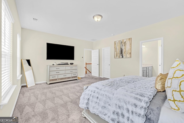 bedroom with connected bathroom, light carpet, and multiple windows