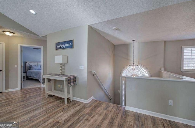 hall with wood-type flooring, a textured ceiling, lofted ceiling, and a notable chandelier