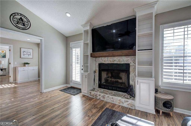 living room with hardwood / wood-style flooring, a large fireplace, a textured ceiling, and vaulted ceiling