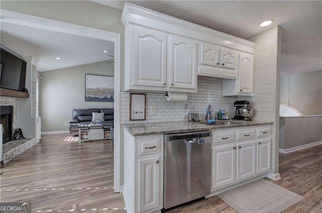 kitchen with stainless steel dishwasher, a textured ceiling, a fireplace, white cabinetry, and lofted ceiling