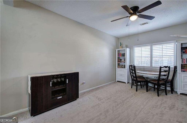 dining area with a textured ceiling, light colored carpet, and ceiling fan