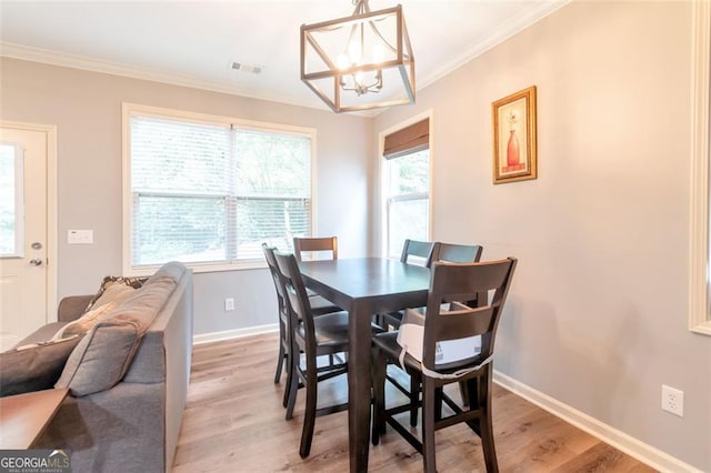 dining area featuring light wood-type flooring, ornamental molding, and an inviting chandelier