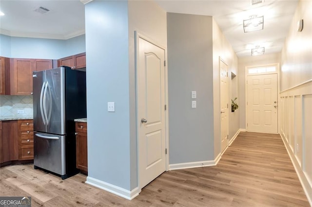 kitchen with backsplash, stainless steel fridge, light wood-type flooring, ornamental molding, and light stone counters