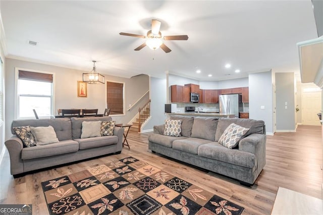 living room with ceiling fan with notable chandelier, light hardwood / wood-style floors, and ornamental molding