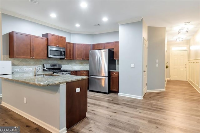 kitchen with light stone counters, sink, stainless steel appliances, and light hardwood / wood-style floors