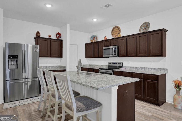 kitchen with stainless steel appliances, sink, light hardwood / wood-style floors, an island with sink, and dark brown cabinets