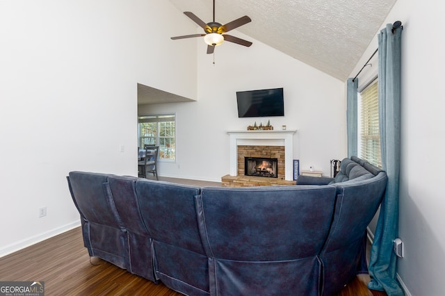 living room with ceiling fan, a stone fireplace, dark hardwood / wood-style floors, lofted ceiling, and a textured ceiling