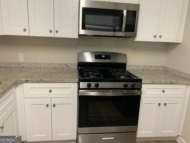 kitchen with appliances with stainless steel finishes, white cabinetry, and light stone counters