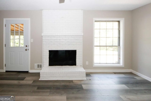 unfurnished living room with a fireplace, dark hardwood / wood-style flooring, and a healthy amount of sunlight