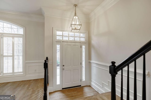 foyer featuring light hardwood / wood-style floors, ornamental molding, and a notable chandelier