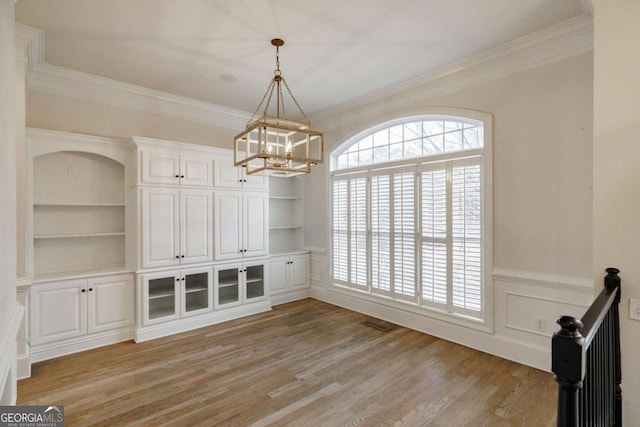 unfurnished dining area with built in features, an inviting chandelier, ornamental molding, and light hardwood / wood-style flooring