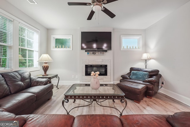 living room featuring ceiling fan, light hardwood / wood-style floors, and a tiled fireplace