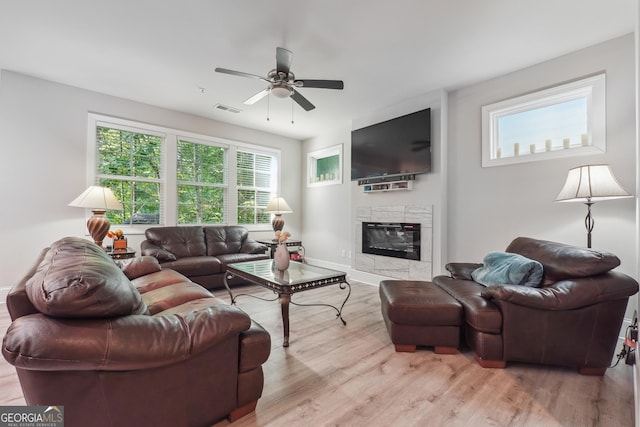 living room featuring ceiling fan, a fireplace, and light wood-type flooring