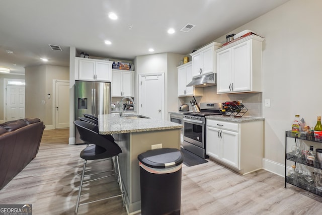 kitchen with light wood-type flooring, stainless steel appliances, a center island with sink, and sink