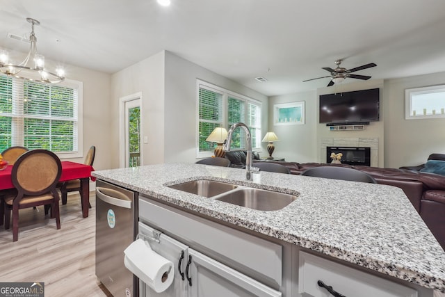 kitchen with ceiling fan with notable chandelier, sink, stainless steel dishwasher, decorative light fixtures, and light stone counters