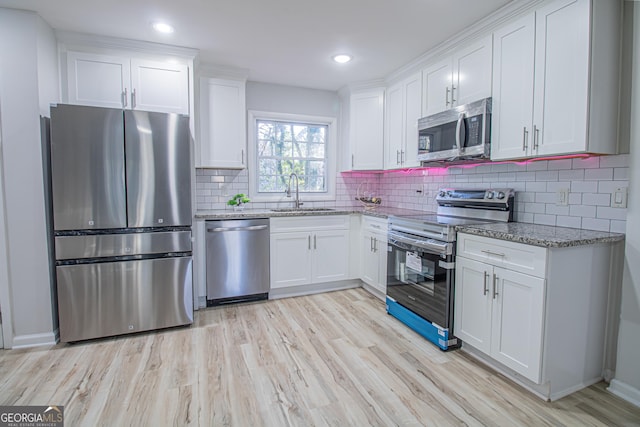 kitchen with light stone counters, stainless steel appliances, sink, light hardwood / wood-style floors, and white cabinetry