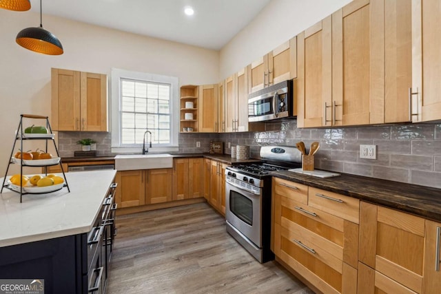 kitchen with sink, tasteful backsplash, dark stone counters, appliances with stainless steel finishes, and light wood-type flooring