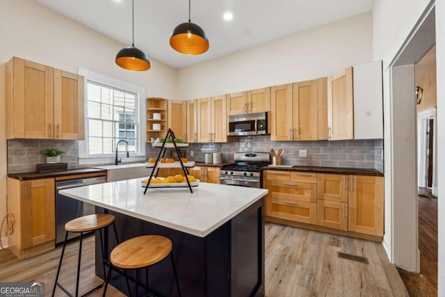 kitchen featuring stainless steel appliances, tasteful backsplash, decorative light fixtures, a kitchen island, and light wood-type flooring