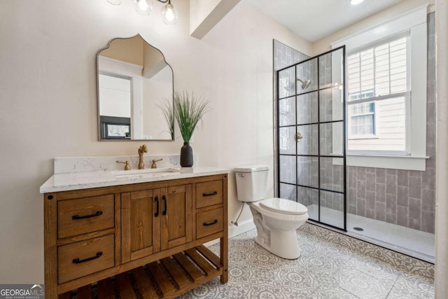 bathroom with a tile shower, vanity, toilet, and a healthy amount of sunlight