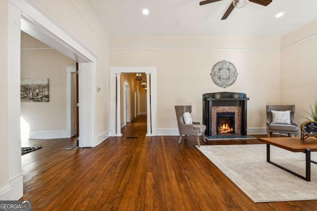 living room featuring a stone fireplace, ceiling fan, and dark hardwood / wood-style floors